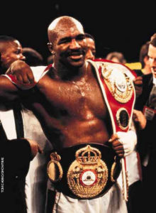 Evander Holyfield celebrating win with title belts
